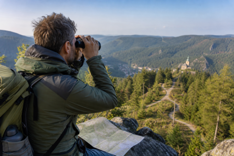 Wanderer erkennt mit einem Fernglas Landmarken in einem bewaldeten Tal