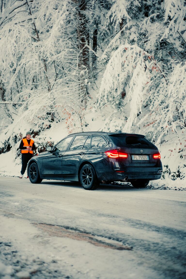 Person hilft einem im Schnee festgefahrenen Auto auf einer Waldstraße im Winter