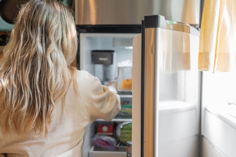 Frau nimmt Lebensmittel aus einem geöffneten Kühlschrank in einer hellen Küche