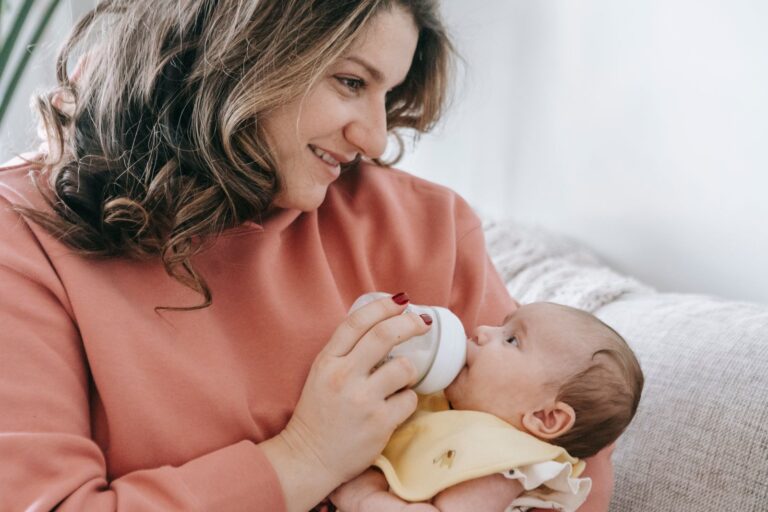 Mutter füttert ein Baby mit dem Fläschchen auf dem Sofa