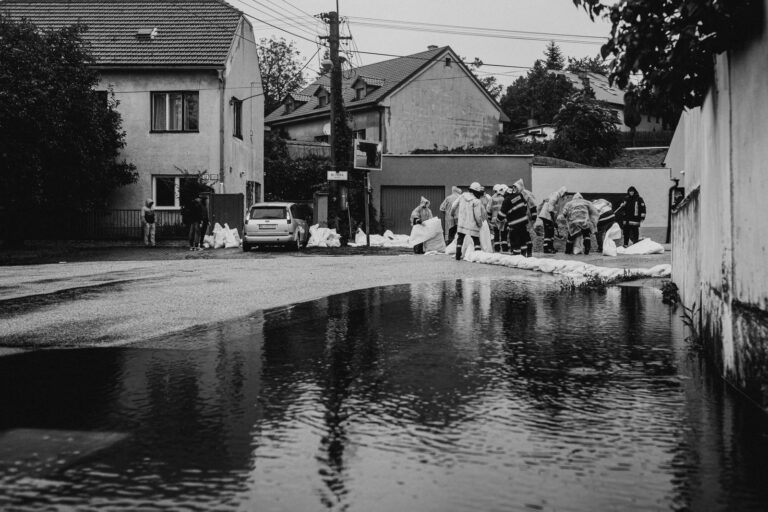 Helfer in Regenkleidung bauen eine Sandsackbarriere in einer überfluteten Wohnstraße
